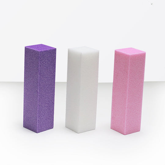 3 blocs polissoirs violet, blanc et rose posés côte à côte sur un sol gris, un mur blanc est derrière