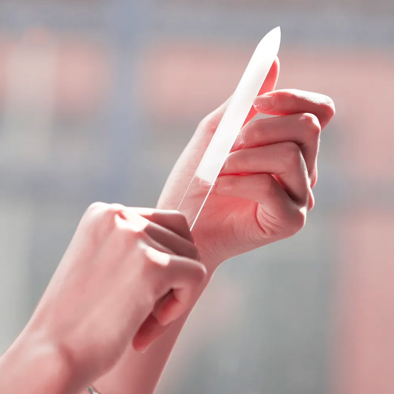 une femme utilise la lime à ongle en verre sur sa main, fond en flou gaussien